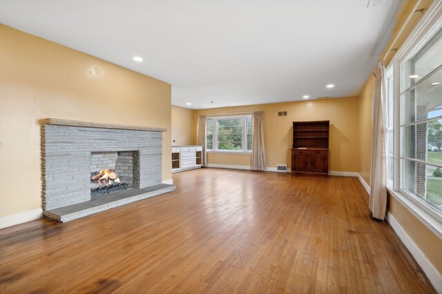 unfurnished living room featuring baseboards, visible vents, wood finished floors, and a stone fireplace