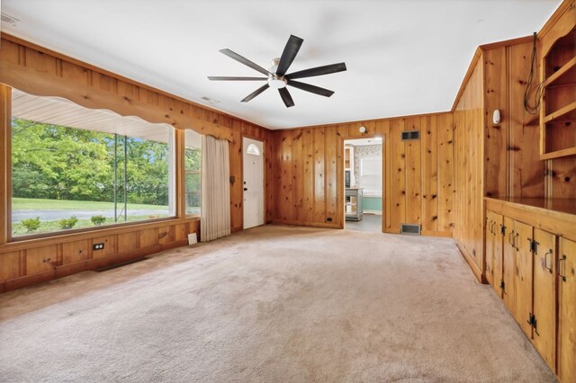 empty room with wood walls, visible vents, a ceiling fan, and light colored carpet