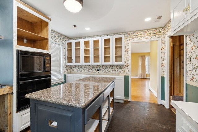 kitchen featuring black appliances, glass insert cabinets, wallpapered walls, and a center island