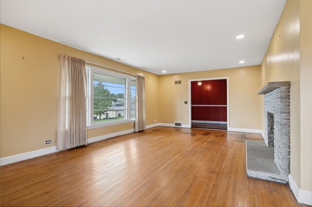 unfurnished living room featuring baseboards, visible vents, a fireplace with raised hearth, wood finished floors, and recessed lighting