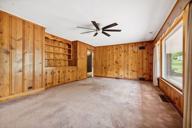 spare room with light carpet, ceiling fan, visible vents, and wooden walls