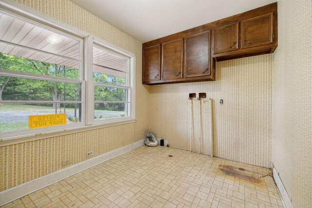 laundry area featuring wallpapered walls, brick patterned floor, baseboards, and cabinet space