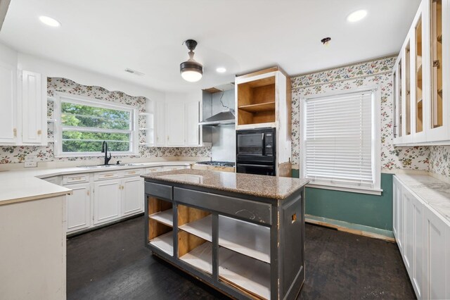 kitchen with white cabinets, wall chimney range hood, black appliances, open shelves, and a sink