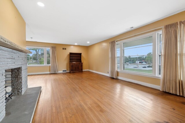 unfurnished living room with light wood-style floors, a brick fireplace, visible vents, and baseboards