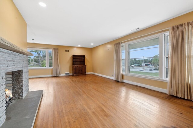 unfurnished living room featuring a brick fireplace, visible vents, light wood-style flooring, and baseboards