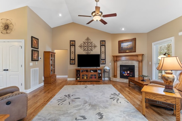 living room with visible vents, a tiled fireplace, wood finished floors, baseboards, and vaulted ceiling