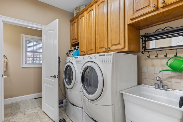 washroom with cabinet space, separate washer and dryer, baseboards, and a sink