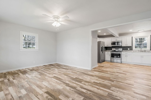 kitchen featuring stainless steel appliances, open floor plan, white cabinetry, a sink, and light wood-type flooring