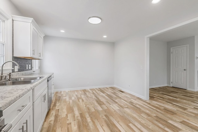 kitchen with stainless steel dishwasher, white cabinetry, light countertops, and a sink