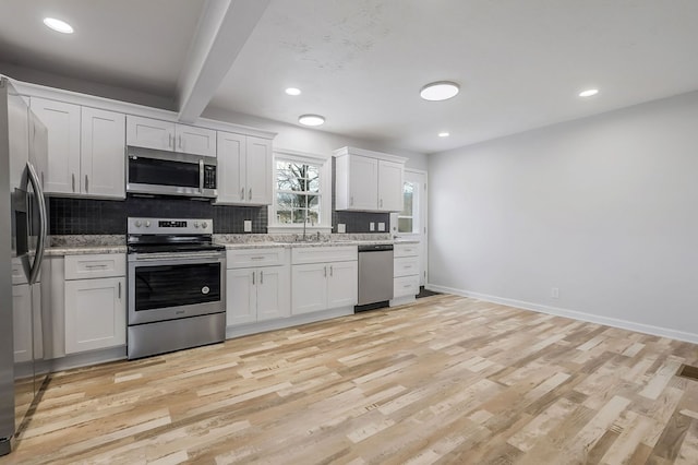 kitchen featuring tasteful backsplash, light wood-style flooring, appliances with stainless steel finishes, white cabinets, and baseboards