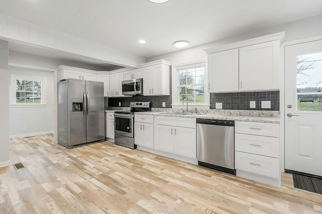 kitchen with white cabinets, decorative backsplash, light stone countertops, stainless steel appliances, and a sink