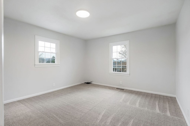 carpeted spare room with a healthy amount of sunlight, visible vents, and baseboards