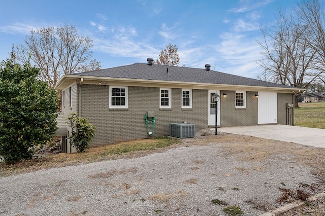 rear view of house with concrete driveway, central AC, and brick siding