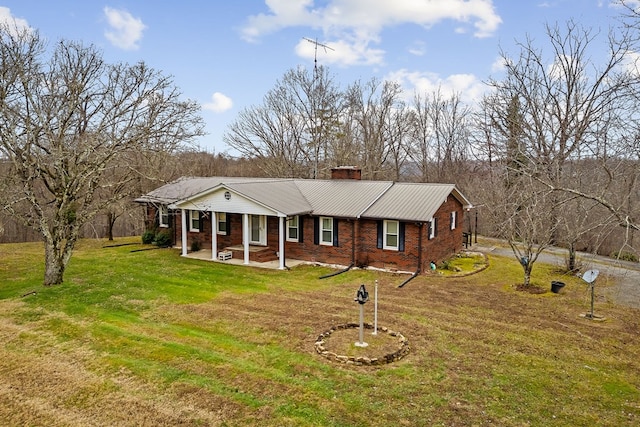 view of front of property with brick siding, a chimney, metal roof, covered porch, and a front yard