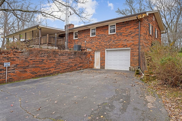 view of side of home with brick siding, a chimney, central AC, a garage, and driveway