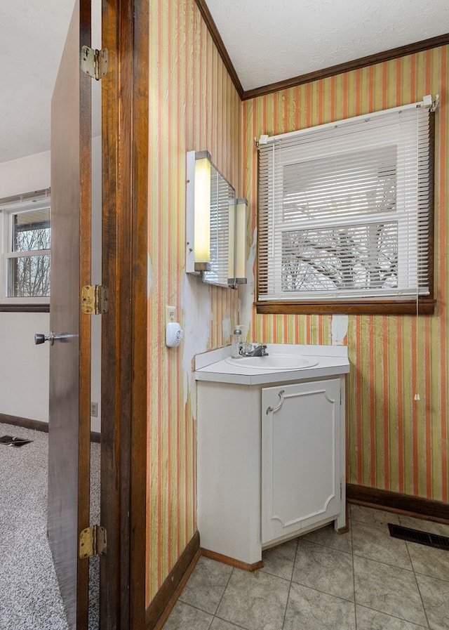 bathroom featuring visible vents, baseboards, vanity, ornamental molding, and wallpapered walls