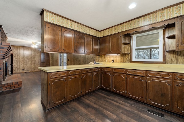 kitchen featuring visible vents, dark wood-type flooring, a peninsula, light countertops, and a fireplace