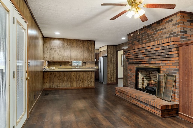 kitchen with dark wood finished floors, freestanding refrigerator, a peninsula, light countertops, and a fireplace