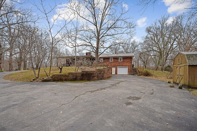 exterior space featuring brick siding, driveway, a chimney, and an attached garage