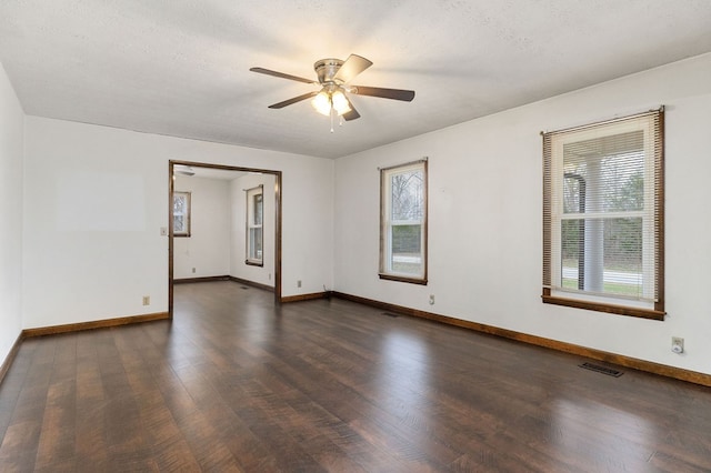 empty room featuring dark wood finished floors, visible vents, plenty of natural light, and baseboards