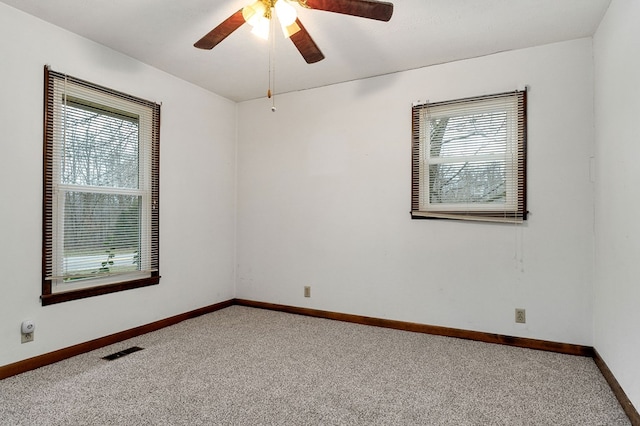 empty room with carpet floors, a ceiling fan, visible vents, and baseboards