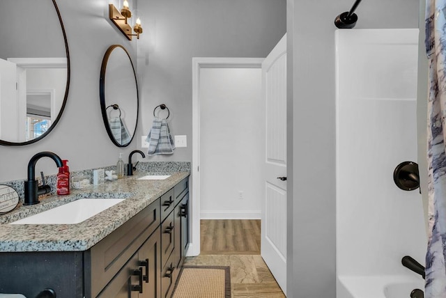 bathroom featuring shower / bathtub combination, double vanity, a sink, and baseboards