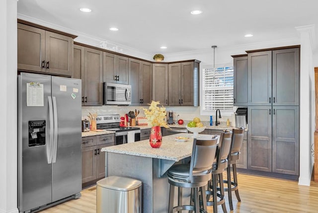 kitchen featuring light stone counters, hanging light fixtures, stainless steel appliances, crown molding, and light wood-type flooring