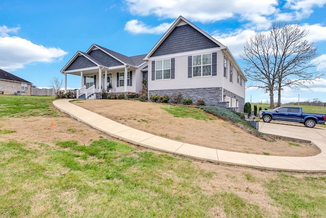 view of front of home with a front lawn, covered porch, stone siding, and concrete driveway