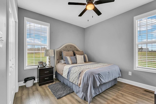 bedroom featuring multiple windows, light wood-type flooring, visible vents, and baseboards