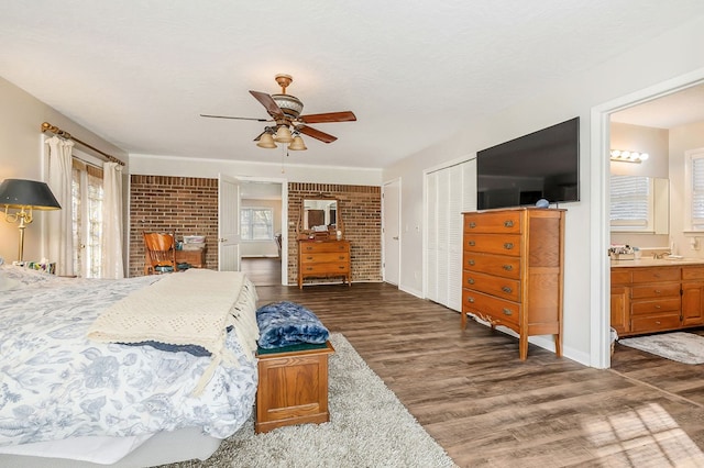 bedroom featuring a ceiling fan, connected bathroom, dark wood-style floors, brick wall, and a closet