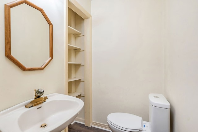 half bath featuring baseboards, a sink, toilet, and wood finished floors