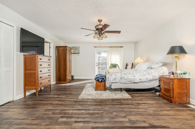 bedroom featuring a wall unit AC, a textured ceiling, baseboards, and wood finished floors