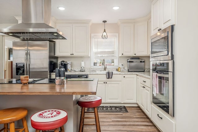 kitchen with wall chimney exhaust hood, stainless steel appliances, wood finished floors, and a kitchen breakfast bar