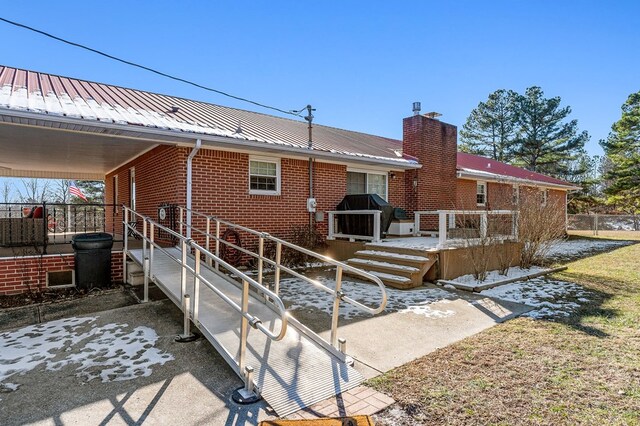 rear view of property with brick siding, metal roof, and a chimney