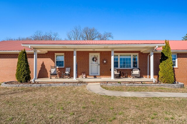 ranch-style home featuring a front yard, covered porch, brick siding, and metal roof