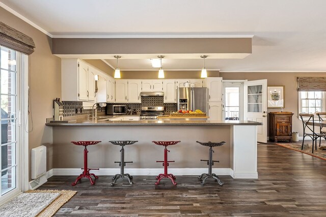 kitchen featuring a peninsula, a sink, white cabinetry, hanging light fixtures, and appliances with stainless steel finishes