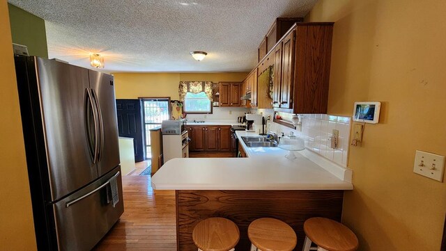 kitchen with a breakfast bar area, a peninsula, light countertops, freestanding refrigerator, and brown cabinets