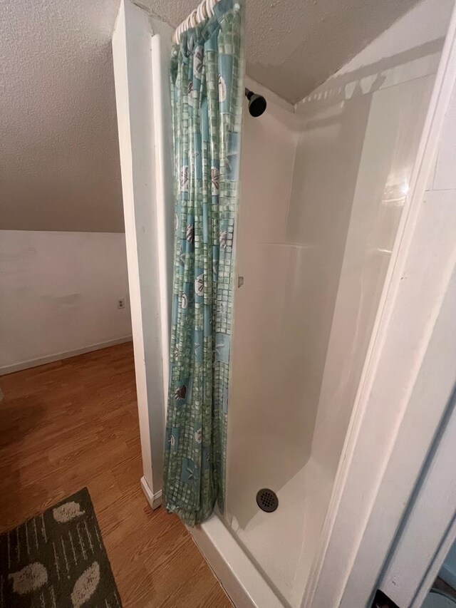 full bathroom with a textured ceiling, lofted ceiling, wood finished floors, baseboards, and a shower stall