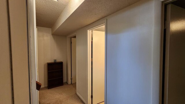 hallway featuring light carpet, a textured ceiling, and baseboards