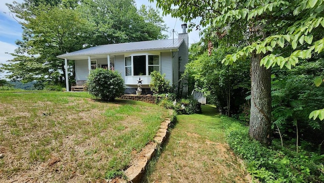 view of front of house featuring metal roof, a porch, a chimney, and a front yard