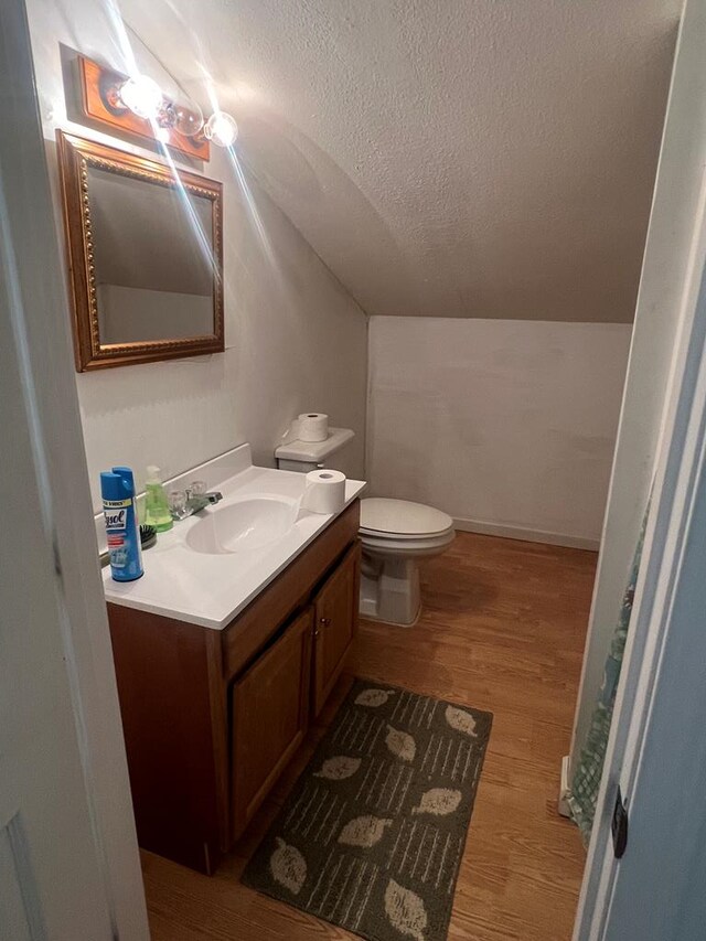 bathroom with lofted ceiling, toilet, wood finished floors, a textured ceiling, and vanity