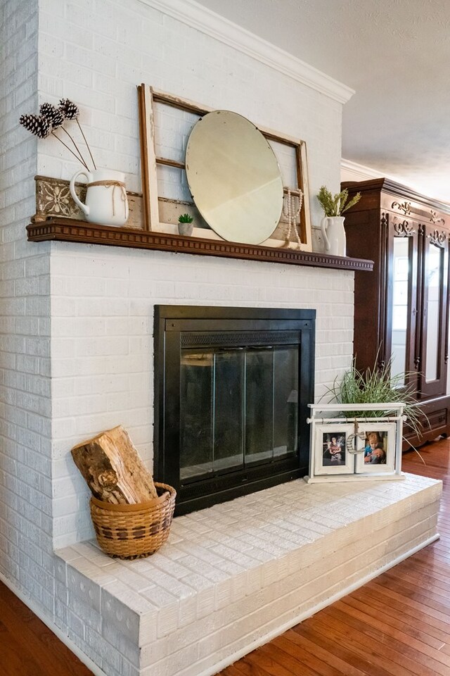 interior details with ornamental molding, a brick fireplace, and wood finished floors