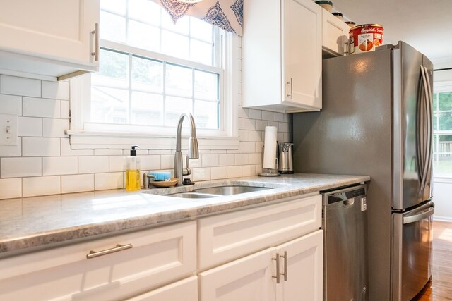 kitchen featuring light stone counters, backsplash, stainless steel dishwasher, white cabinetry, and a sink