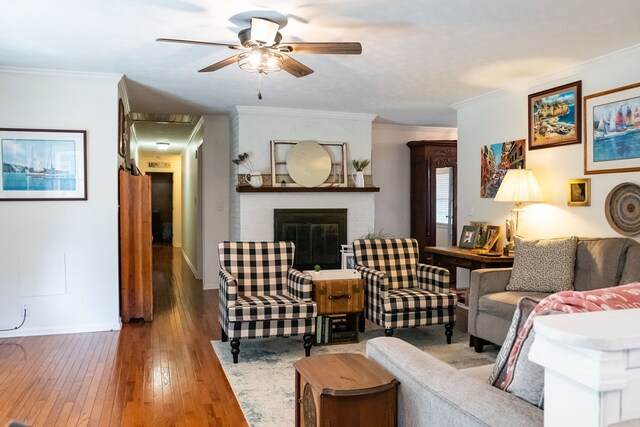 living room with a brick fireplace, wood finished floors, a ceiling fan, and crown molding