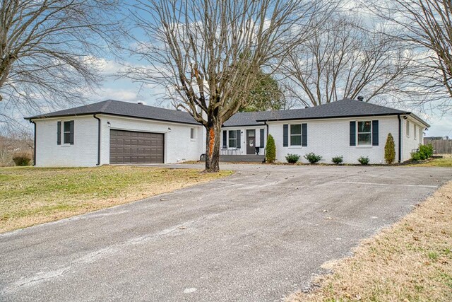 ranch-style house with an attached garage, a front yard, aphalt driveway, and brick siding