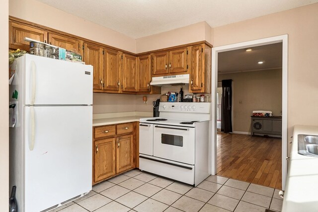 kitchen featuring white appliances, light tile patterned floors, brown cabinetry, light countertops, and under cabinet range hood