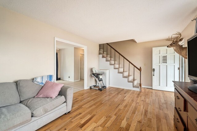 living room featuring baseboards, stairway, light wood finished floors, and a textured ceiling