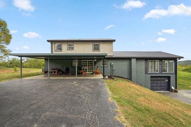 view of front of house with metal roof, brick siding, driveway, and a front lawn