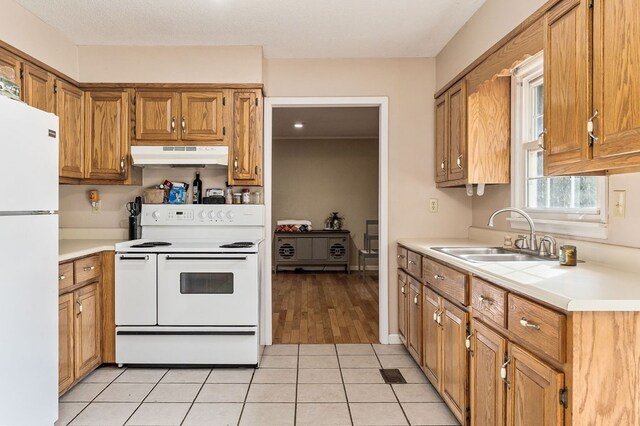 kitchen featuring light countertops, white appliances, a sink, and under cabinet range hood