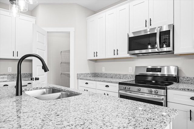 kitchen featuring appliances with stainless steel finishes, a sink, light stone counters, and white cabinets